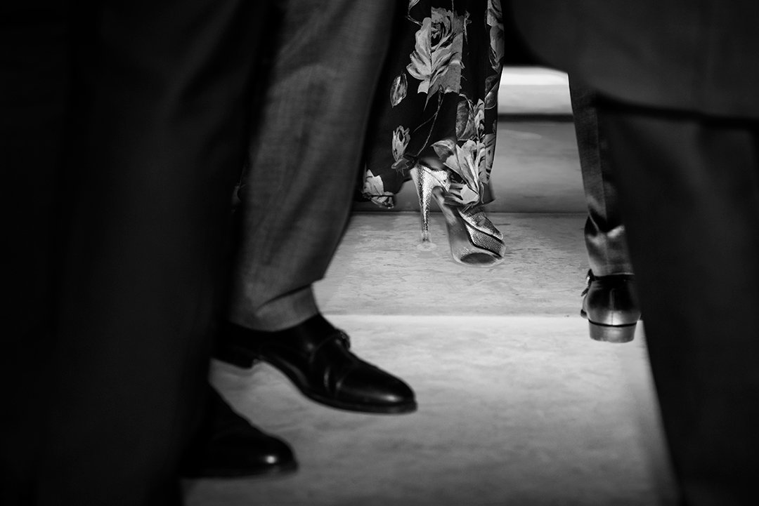 Shoes and legs frame other feet in the background.